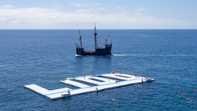 Swimmers at a floating sea platform off the Funchal Lido, with a tall ship beyond, Madeira